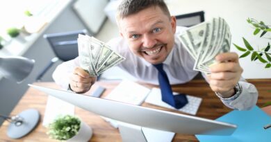 Homem sorridente segurando um maço de dinheiro na frente de um laptop aberto, demonstrando o conceito de ganhos rápidos online.