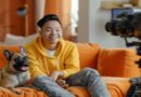 Um jovem criador de conteúdo sorridente, gravando um vídeo em seu estúdio caseiro, com um laptop e um microfone à sua frente.
