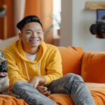 Um jovem criador de conteúdo sorridente, gravando um vídeo em seu estúdio caseiro, com um laptop e um microfone à sua frente.